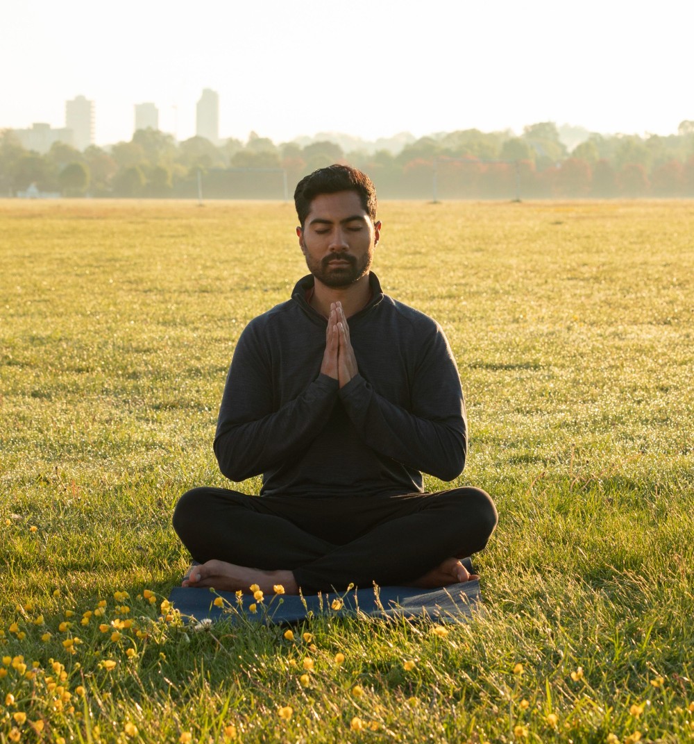 A man meditating in a grassy park at sunrise